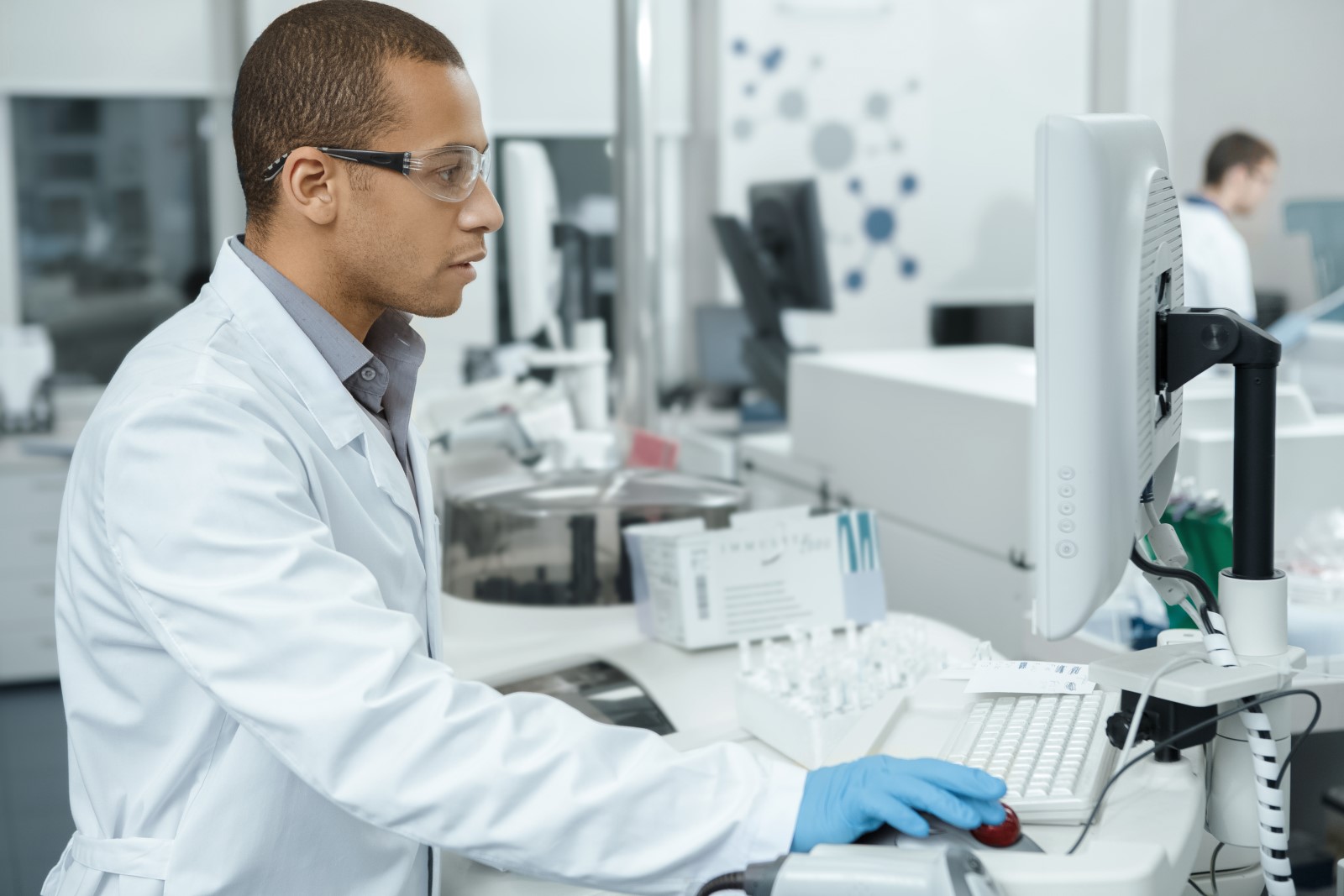 a man in a lab coat works in a lab using syringes and a computer.